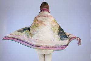 Person wearing a large, colorful scarf draped over their shoulders against a plain background